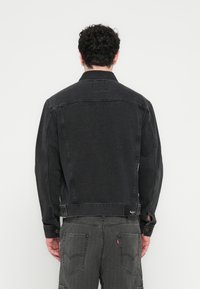 Črna jakna iz jeansa s klasičnim ovratnikom, vidnim šivanjem in dvema stranskima žepoma. Prilegajoč se dizajn z teksturirano površino in znamčno etiketo.