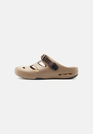 Hellbraune Slip-On-Sandale mit ausgeschnittenen Belüftungslöchern und einem verstellbaren dunkelbraunen Riemen oben für sicheren Halt.