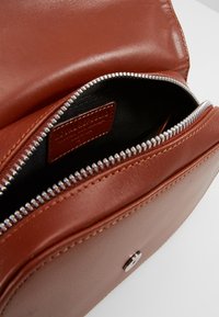 Bolso de cuero marrón con un zipper plateado, con textura suave y un interior oscuro. Interior etiquetado con una etiqueta de la marca visible.
