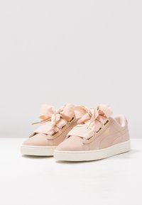 Baskets en daim rose avec grands nœuds en satin, accents dorés, semelles blanches en caoutchouc et texture lisse. Design léger et profil bas.