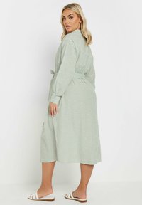 Randig grön midi-klänning i ett lätt material med långa ärmar, knytmidja och sidofickor, kombinerad med vita slidesandaler.