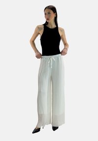 White pleated trousers with an elastic waistband and drawstring, paired with a black sleeveless top and black pointed shoes.