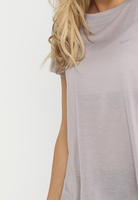 Camiseta de cuello redondo de color gris claro, hecha de una tela suave y ligera. Presenta mangas cortas y un sutil logo de Nike en la parte superior izquierda.