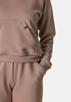 Hanorac bej deschis cu un buzunar mare în față, manșoane ribbate și pantaloni tapered asortați. Textură netedă, design minimalist, fără modele.