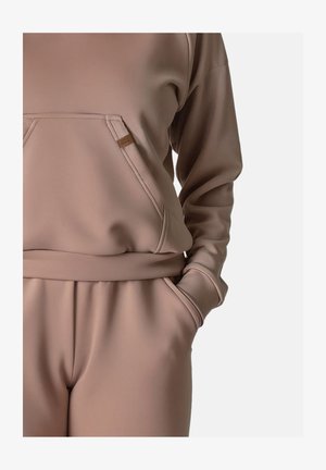 Světlobéžová mikina s velkou přední kapsou, žebrovanými manžetami a odpovídajícími zúženými kalhotami. Hladká textura, minimalistický design, bez vzorů.