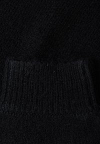 Närbild av svart stickad tyg med ribbstruktur och veckad kant, som visar detaljerade ullfibrer och sömmönster.