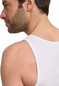 Canotta bianca in cotone con spalline larghe, caratterizzata da una texture liscia e morbida e da un design semplice. Mostra il retro di una figura maschile.