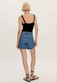 Body negro, pantalones cortos de mezclilla azul. Los pantalones cortos tienen una cintura alta, bolsillos y un dobladillo deshilachado. La modelo lleva sandalias negras con tiras.