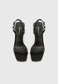 Μαύρα σανδάλια ψηλοτάκουνα με τετράγωνη μύτη, λείο δερμάτινο υλικό, λεπτά λουριά στον αστράγαλο και ασημένια αγκράφα. Ορατή η σήμανση Michael Kors.