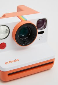 Polaroid instant camera in orange and white. Features a circular lens, red buttons, and a rainbow stripe on the top. Compact rectangular shape.