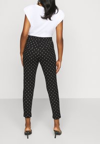 Černé kalhoty s puntíky, které mají fitted střih, pružný pas a kapsy. Doplněné bílým topem s krátkými rukávy a černými podpatkovými muly.