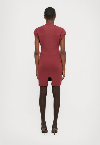 Maroon bodycon dress with short sleeves and shoulder accents, ribbed texture, knee-length with a back slit. Worn with dark tights and heels.