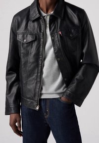 Giacca in pelle nera con tasche sul petto con bottoni, colletto classico e hardware argentato. Abbinata a un maglione grigio e jeans blu.