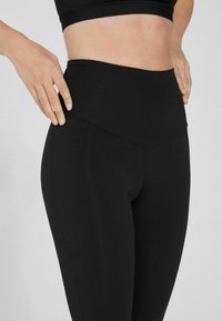 Leggings noirs taille haute en tissu extensible et lisse, avec un design sans couture et de subtils détails de coutures courbées.