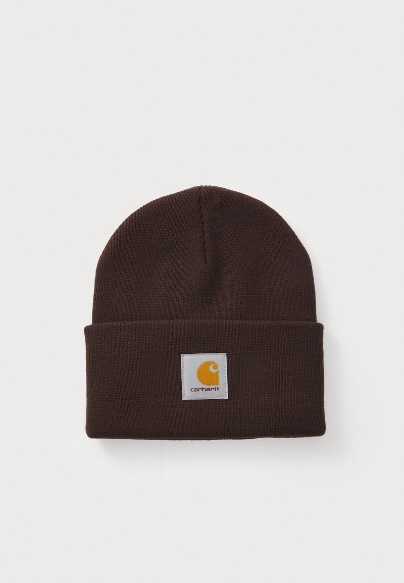 Brown knit beanie with a folded cuff, featuring a square white label with a yellow logo. Soft, textured fabric suitable for warmth.
