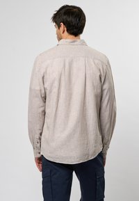 Camisa de manga larga color beige claro con un patrón texturizado, dobladillo curvado y puños abotonados. Presenta un yugo trasero y un cuello clásico.