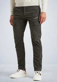 Pantalons cargo en coton mélangé vert foncé, avec de multiples poches, des jambes fuselées et une finition texturée, portés avec des baskets blanches.