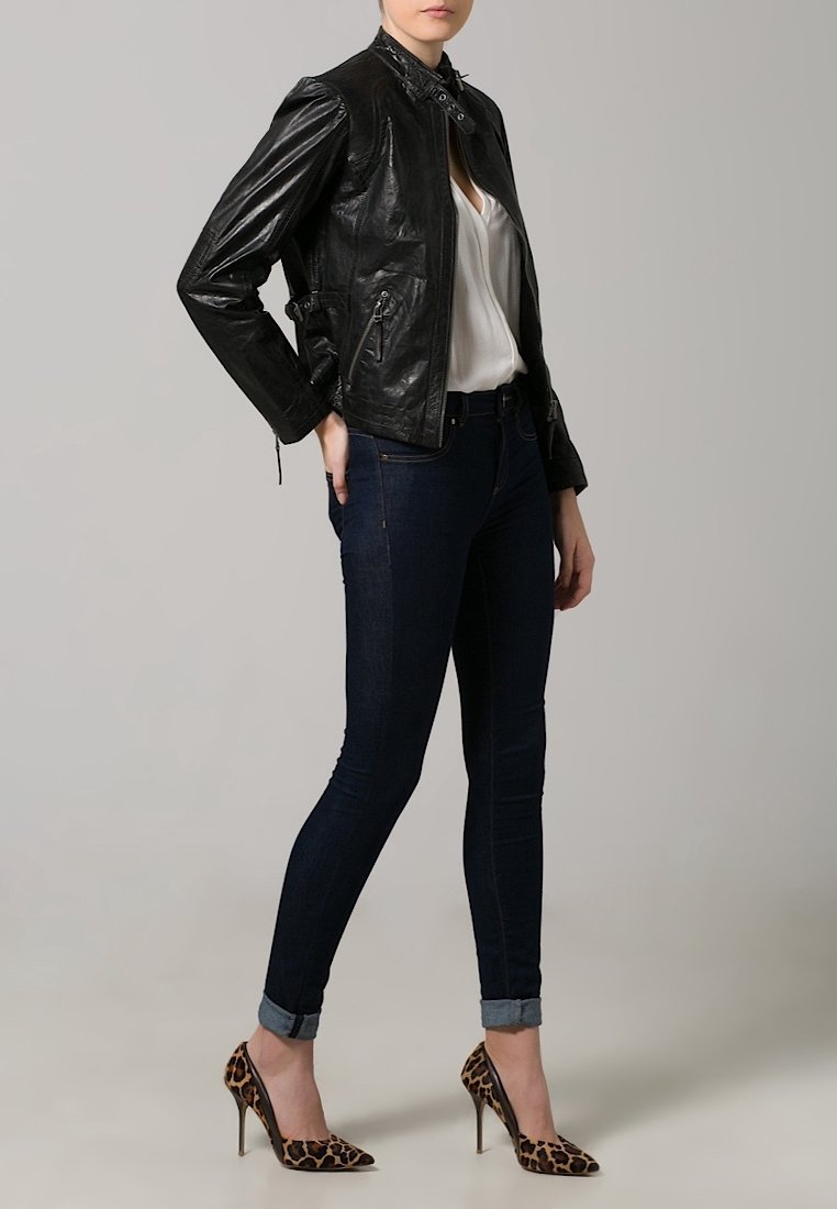 Giubbotto di pelle nera con colletto alto, abbinato a una camicia bianca, jeans di denim scuro e tacchi alti con stampa leopardata.