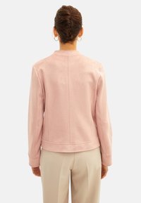 Jasnoróżowa zamszowa kurtka o dopasowanym kroju, z prążkowanymi mankietami i okrągłym dekoltem. Szw na plecach dodaje subtelnej faktury.