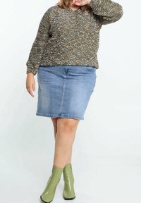 Teksturowany zielono-brązowy sweter z długimi rękawami, zestawiony z spódnicą z niebieskiego denimu do kolan i zielonymi botkami za kostkę z ostrym noskiem.