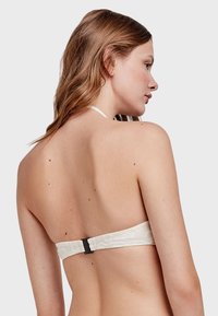Witte bandeau bikini top met een textuurdesign, voorzien van een zwarte sluiting aan de achterkant. Strakke lijnen en minimale bedekking.