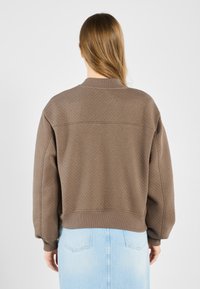 Brown quilted sweatshirt with a stand-up collar, drop shoulders, and ribbed cuffs, paired with a light blue denim skirt.