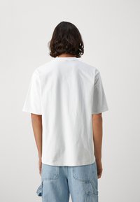Weißes Baumwoll-T-Shirt mit kurzen Ärmeln und rundem Halsausschnitt, das eine einfache, glatte Textur aufweist und keine sichtbaren grafischen Designs oder Verzierungen hat.