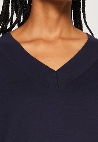 Pull en V bleu marine avec un tissu en tricot texturé, une finition lisse et un subtil détail de couture au niveau de l'encolure.