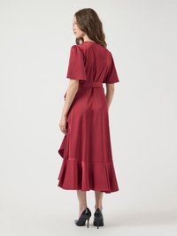 Punainen kietaisumekko lyhyillä puffihihnoilla, rypytetyllä helman reunalla ja vyötäröllä. Silkkinen kangas, jossa on kevyt kiilto, yhdistettynä mustiin korkokenkiin.