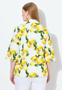 Blusa a maniche corte con motivo di limoni e foglie su sfondo bianco, con vestibilità rilassata e colletto piatto.