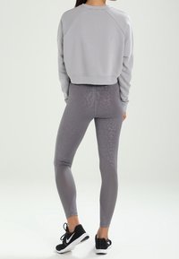 Grijze, kortere sweatshirt met raglanmouwen, gecombineerd met strakke grijze leggings met een subtiel patroon en zwarte sportieve schoenen.
