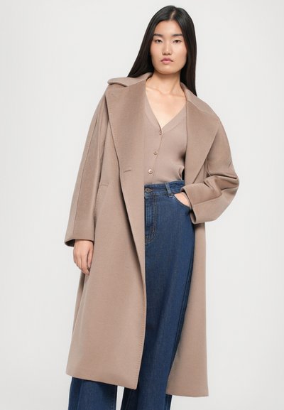 Caban din lână bej cu rever larg și croială relaxată, combinat cu un top cu întreținere ușoară de culoare maro deschis și blugi de tip wide-leg, cu talie înaltă, de culoare albastră.