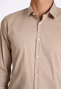 Camicia beige con colletto realizzata in tessuto liscio, caratterizzata da bottoni bianchi, vestibilità regolare e maniche lunghe. Design minimalista senza fantasie.