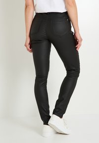 Pantalones ajustados de cuero sintético negros con una textura suave, con bolsillos traseros y una cintura alta, combinados con zapatillas blancas.