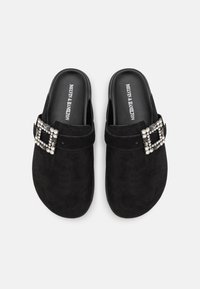 Črne semšaste mule s kvadratno bucko iz rhinestone. Gladka tekstura, zasnova z odprtim hrbtom in ravne podplate. Logotip je odtisan na notranji podplati.