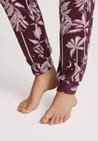 Bordeaux kleurige pyjamabroek met een botanisch patroon van bleekroze palmbladeren en sterren, strakke boorden en een zachte, lichte stof.