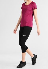 Conjunto deportivo de alto rendimiento que incluye una camiseta ajustada color magenta y unos leggins capri negros, ambos con logos reflectantes de Nike. Zapatillas negras con textura.