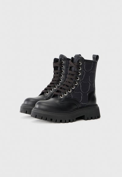 Botas de combate negras con puntera de cuero brillante, paneles de tela texturizada con un patrón ligero, cordones redondos y suelas gruesas y resistentes.
