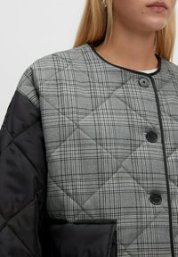 Gequilted geruiten jack in grijs, met een zwarte satijnen mouw, drukknoopsluiting en een ronde halslijn met contrastafwerking.