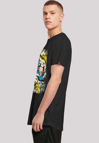 Svart t-skjorte med korte ermer som har et fargerikt grafisk design i tegneserie stil på framsiden, med levende karakterer og detaljerte illustrasjoner.