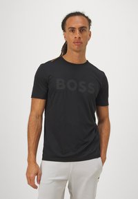 T-shirt noir à manches courtes fabriqué en tissu lisse, arborant un logo "BOSS" ton sur ton bien visible sur la poitrine.