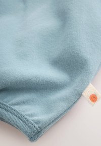 Soft light blue fabric with a ribbed edge and a small white tag featuring an orange circular icon on the lower right corner.