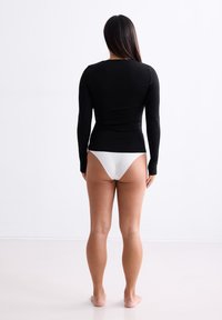 Zwarte top met lange mouwen van stretchy materiaal, gecombineerd met witte bikini onderkant. Glad oppervlak met een strakke pasvorm, minimaal ontwerp.