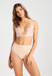 Nude trådlös bh med djup urringning och justerbara remmar, i kombination med högmidjade sömlösa trosor i matchande färg. Mjuk textur.
