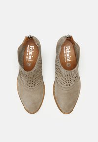 Botines de ante topo con parte superior perforada, puntera afilada y plantilla de cuero marrón. Cuenta con cierre de cremallera en la parte trasera. Tacón de madera semibrillante.