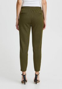 Olivgrön byxor med houndstooth-mönster, i en tajt design, elastisk midja och två bakfickor; bärs med svarta klacksandaler.