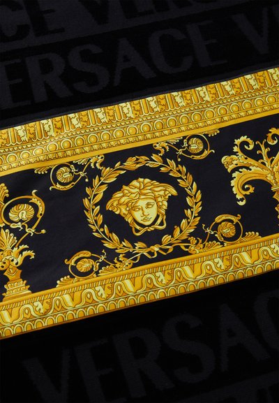 Versace šalis, puikuojantis auksinės ir juodos spalvų deriniu, su centriniu Medūzos motyvu, apsuptu išraiškingų raštų ant lygaus audinio.