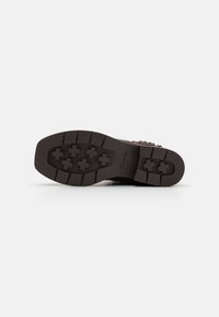 Donkerbruine laarzenzool met diepe profiel, kruisvormige grip en het "Clarks"-logo zichtbaar op een off-white achtergrond.