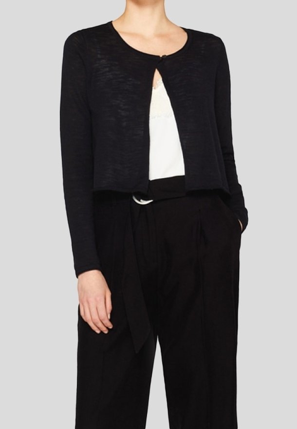 Svart kortärmad kofta, mjukt texturerad tyg, rund halsringning, öppning framtill med en enda knappknäppning, bärs över en vit topp och svarta högmidjade byxor.