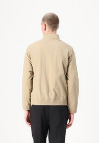 Beige bomberjack met een lichtgewicht, gestructureerde stof. Heeft een hoge kraag, elastische tailleband en raglanmouwen voor een relaxte pasvorm.